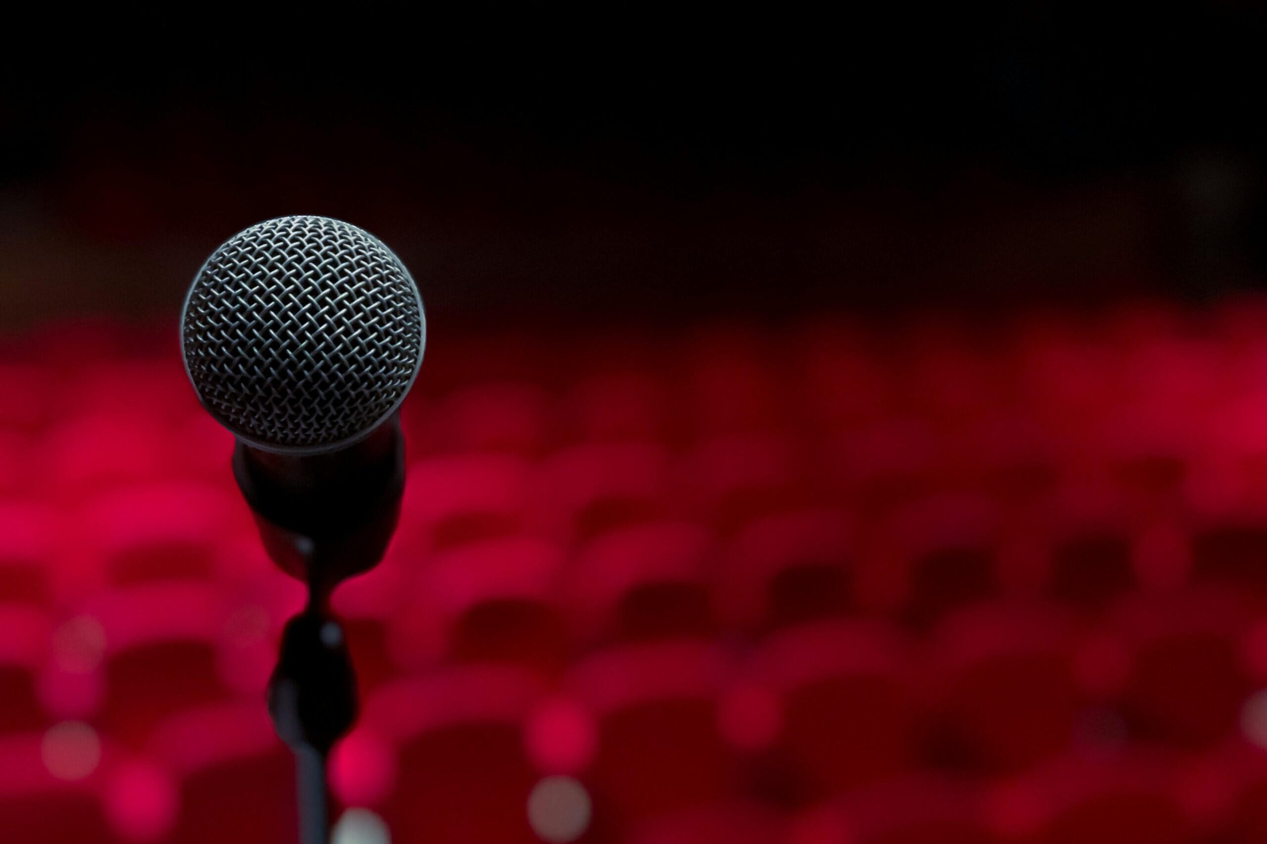 Close-up of microphone on stage with empty red seats in background.
